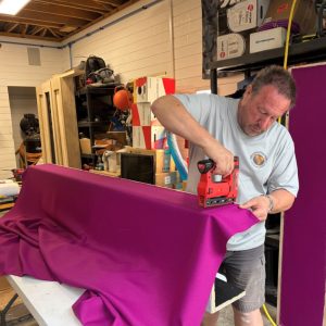 The client's selected color fabric wrap is being applied, adding a custom touch to the theater design.